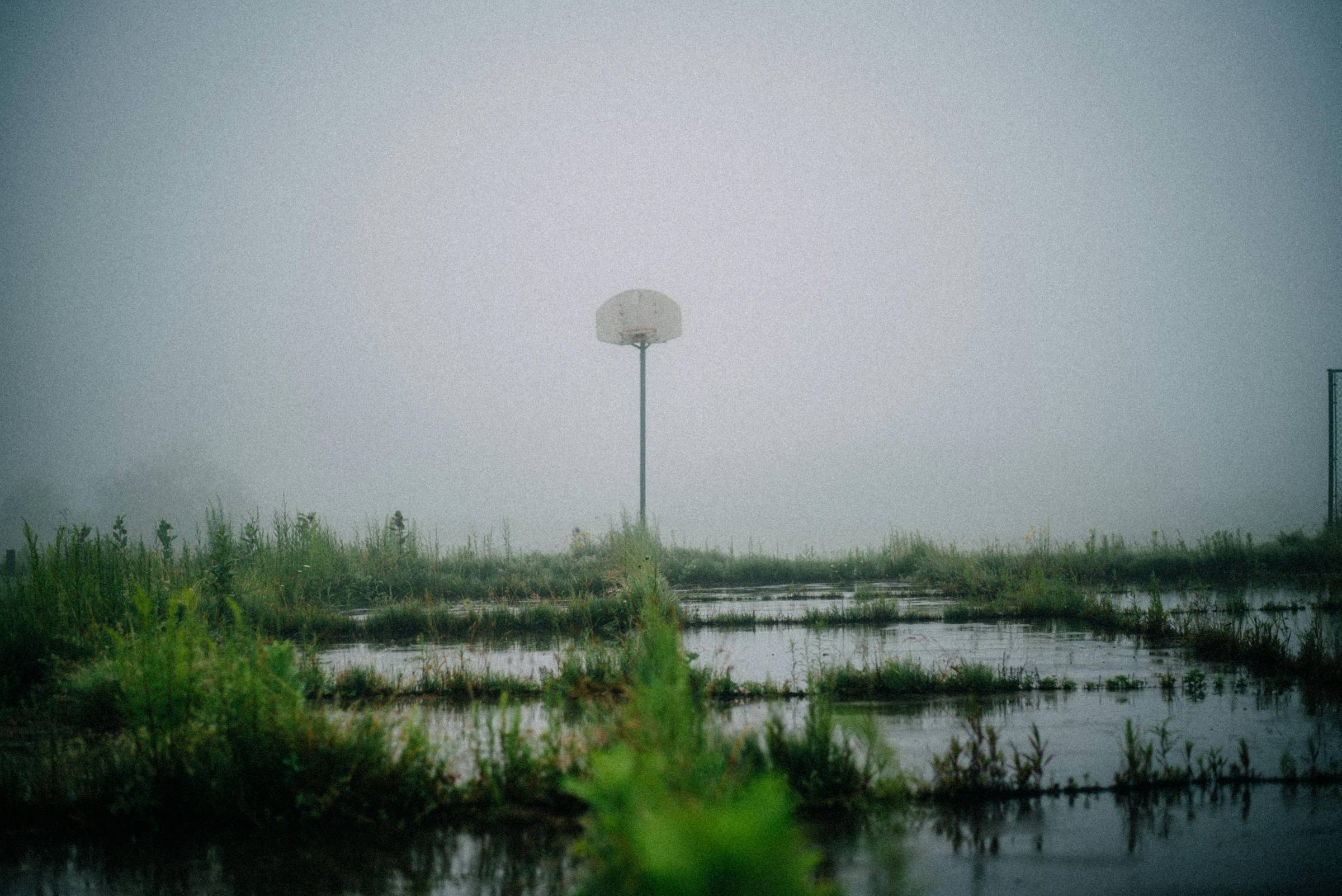 A basketball court is over grown with weeds and being taken over with flood water (credit Harrison Haines)