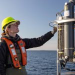 A person is reaching to check on metal bottles that collect ocean water.
