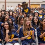 New students in the stands at the welcome day innvcation and pep rally. Students wear their new UM T-Shirt and cheer as Billy the Bison does the same in the background.