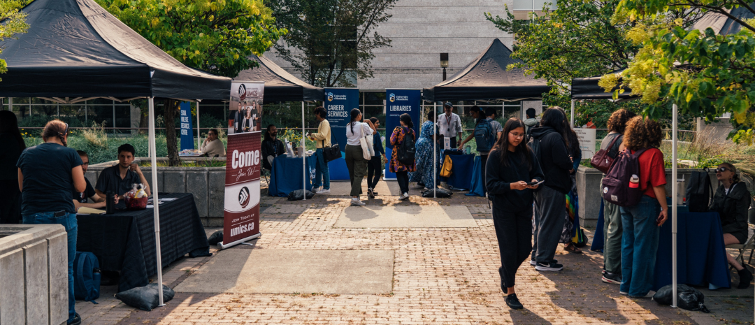 Students visiting outdoor information booths with tents, banners, and tables set up for campus services and clubs.