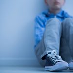 Sad boy in sneakers sits alone in his room.