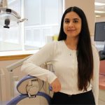 Lala Rukh poses for a photo in the UM dental school's general clinic. She leans against a dental chair and a dental light is behind her.