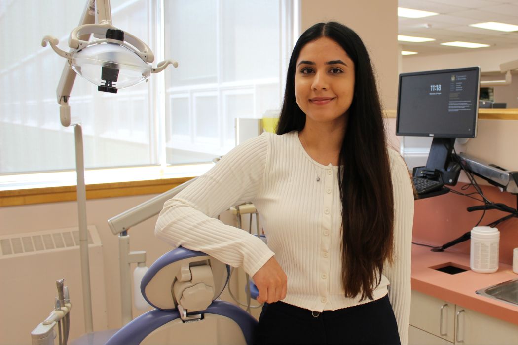 Lala Rukh poses for a photo in the UM dental school's general clinic. She leans against a dental chair and a dental light is behind her.