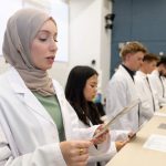 Pharmacy students standing in a row, reading from a program as they recite their pledge of professionalism.