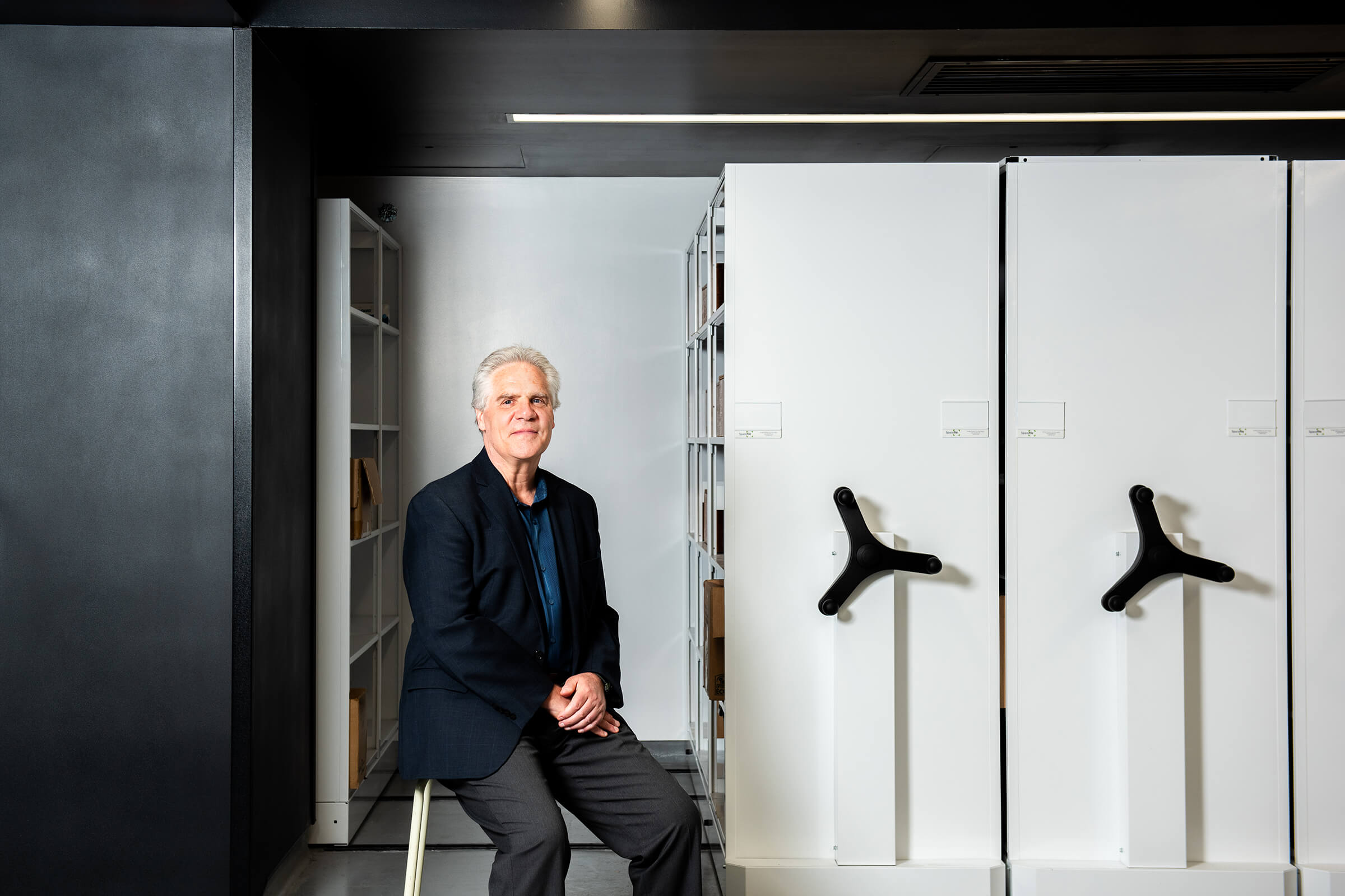 Dr. James Blanchard sitting on a stool in front of rolling filing cabinets