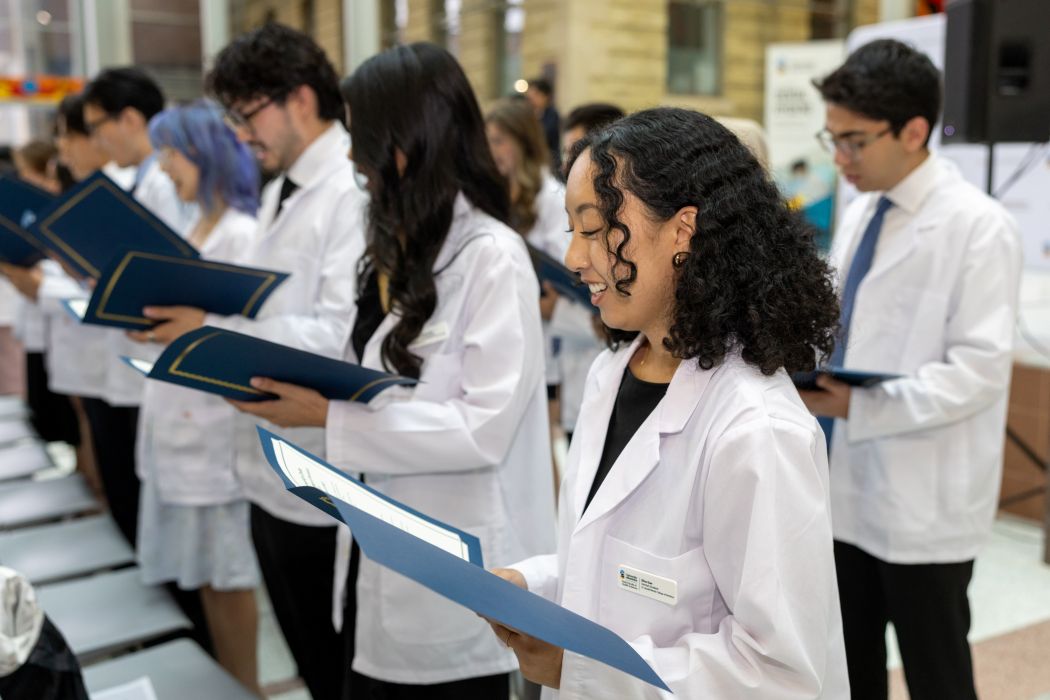 Two rows of students read the Community Code off of papers. They are wearing white coats.