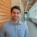Sam Kavosh smiles warmly at the camera while standing in a hallway at the UM Apotex Centre.