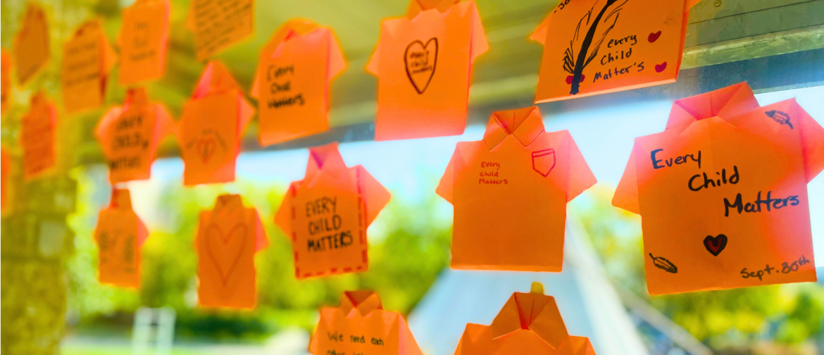 Orange origami shirts with handwritten messages such as 'Every Child Matters' displayed on a window, commemorating the National Day for Truth and Reconciliation.