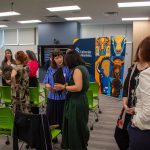 Crowd of people in classroom talking with each other in groups.
