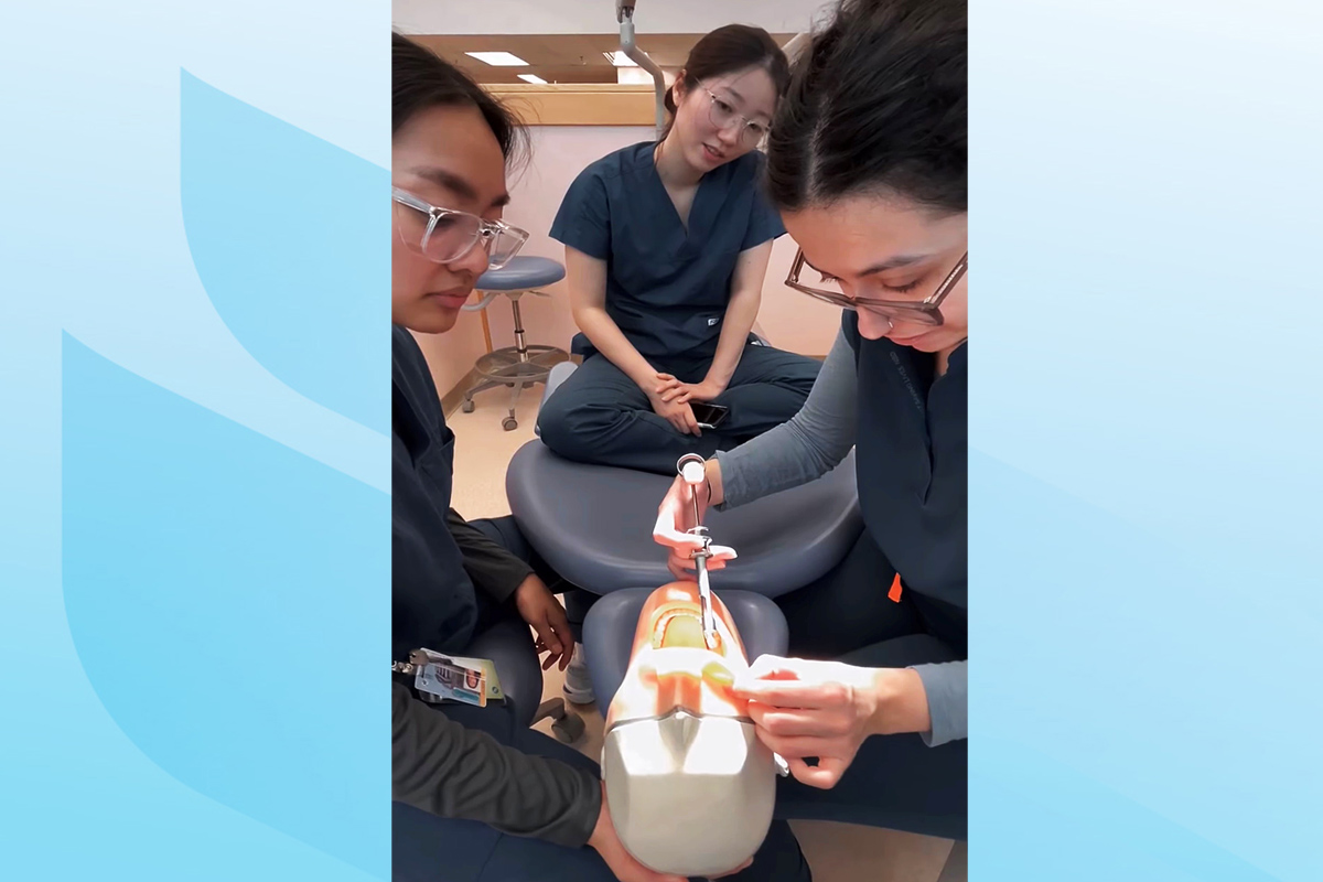 A student practices a procedure on a dentistry mannequin in a dental clinic. Two students watch.