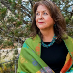 Laura Tohe standing outdoors, wearing a green shawl and turquoise jewelry.