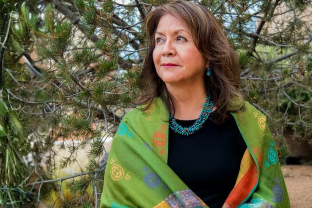 Laura Tohe standing outdoors, wearing a green shawl and turquoise jewelry.