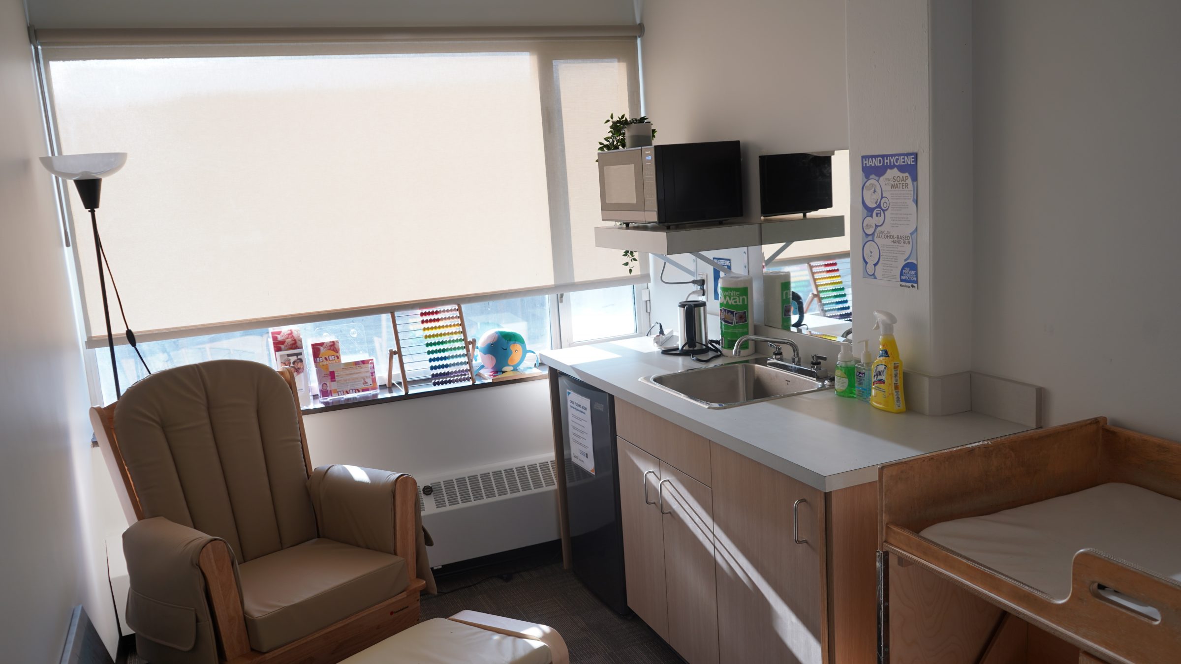 A room with a sink, mini fridge, microwave, change table and large comfortable table with a stool. Toys, posters, resource material and cleaning supplies are also available in this lockable space for child feeding on the UM Fort Garry Campus.