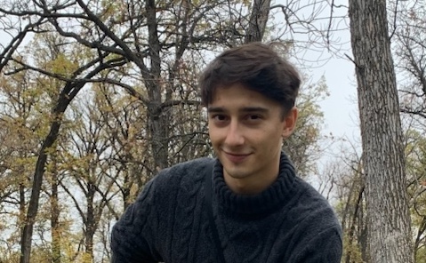 Photo of Riley Parker in a cable-knit sweater in front of trees outdoors