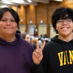 Two attendees smile for the camera at the event, one holding up a peace sign.