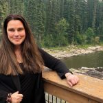 Cherie Murie stands near a river surrounded by trees.