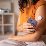 A woman with a continuous glucose monitor on her arm uses her cell phone to check her glucose.