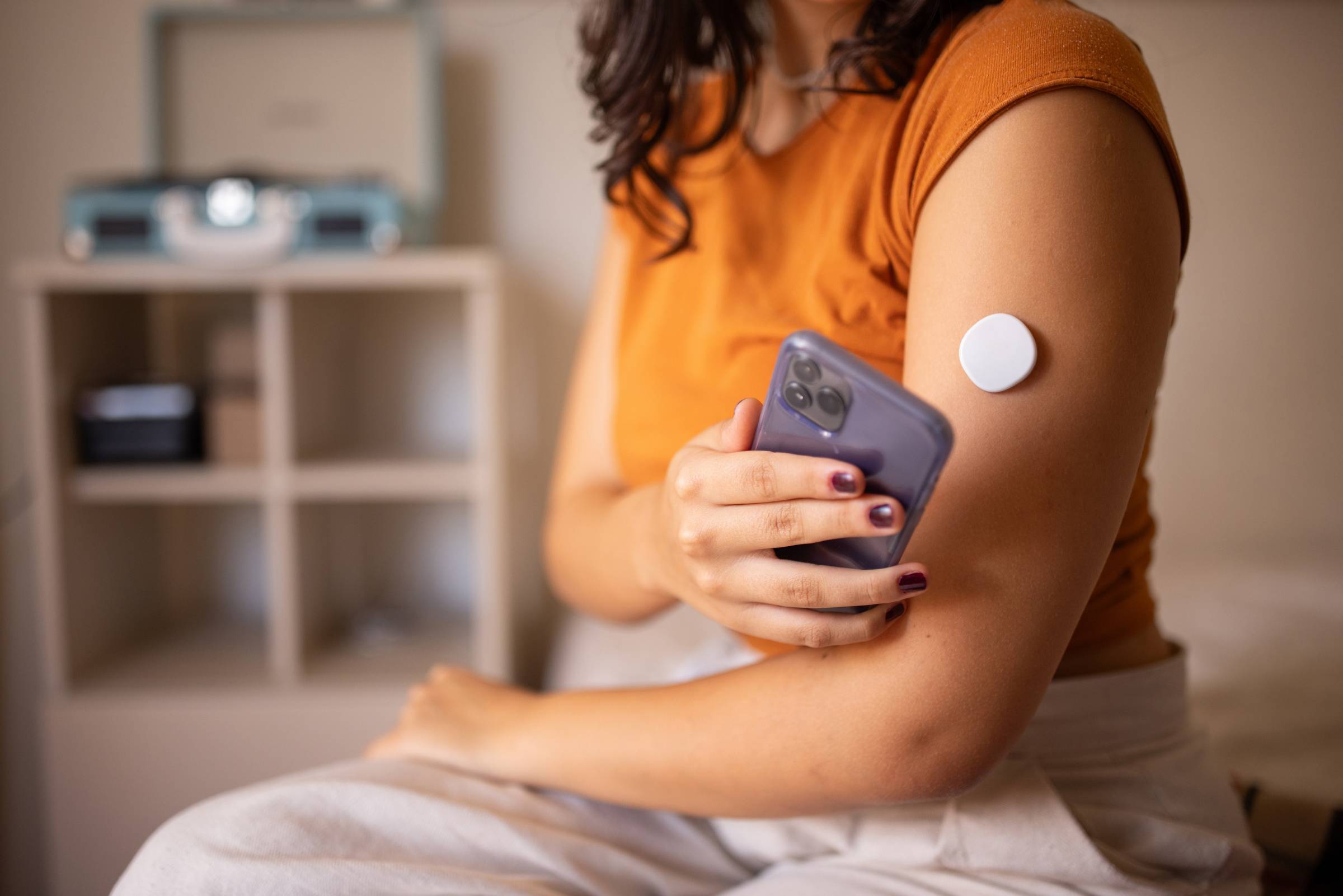 A woman with a continuous glucose monitor on her arm uses her cell phone to check her glucose.