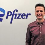 Daryl Fediuk standing and smiling at the camera, with the Pfizer logo in background.