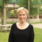 Dr. Judith Scanlan stands outdoors on the Fort Garry campus in summertime.
