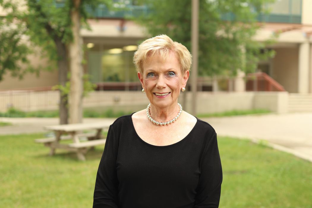 Dr. Judith Scanlan stands outdoors on the Fort Garry campus in summertime.
