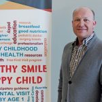 Dr. Bob Schroth next to a banner that reads "Healthy Smile Happy Child." There are also more than 20 terms and words related to oral health on the banner.