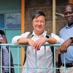 Three people lean against a railing outside a building.