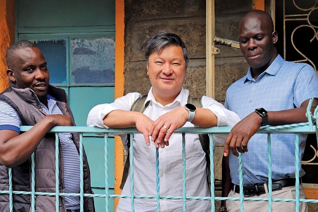 Three people lean against a railing outside a building.