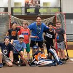 A Mini U leader posing with a group of campers during a floor hockey session.