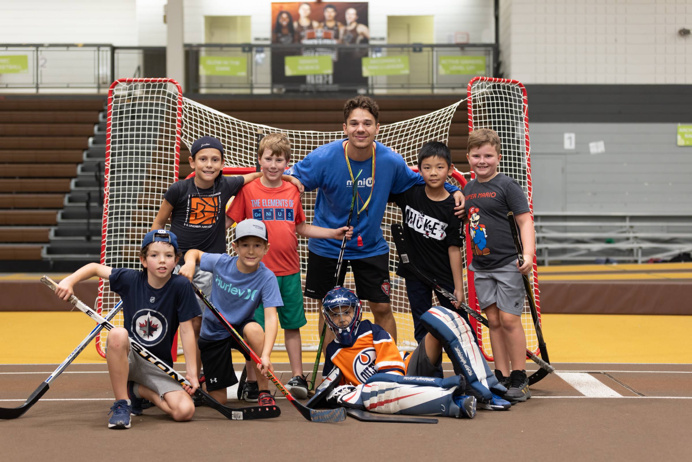 A Mini U leader posing with a group of campers during a floor hockey session.